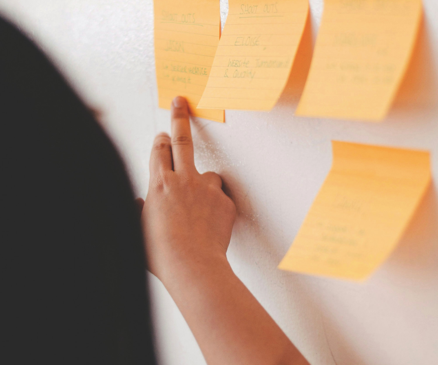 Frau zeigt mit ihrem Finger auf eine Wand voller Post-its