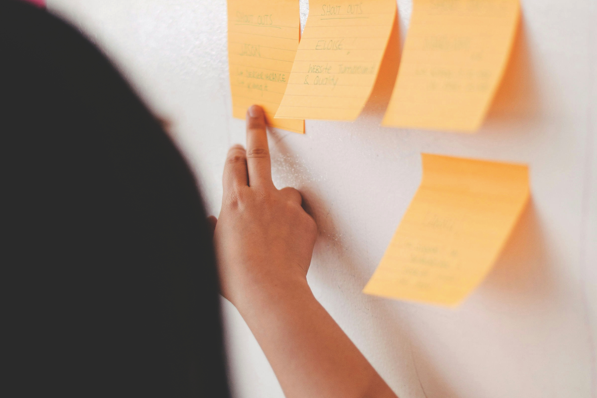 Frau zeigt mit ihrem Finger auf eine Wand voller Post-its